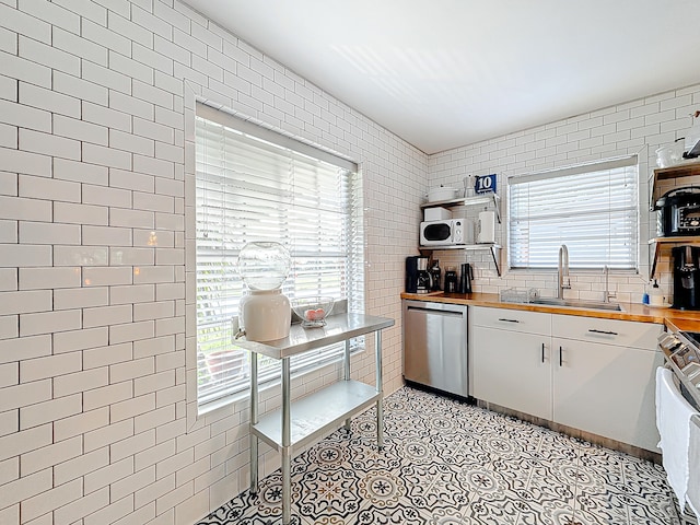 kitchen featuring a wealth of natural light, white cabinets, stainless steel dishwasher, and wood counters