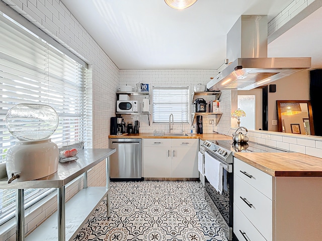 kitchen featuring dishwasher, electric stove, sink, butcher block countertops, and white cabinetry