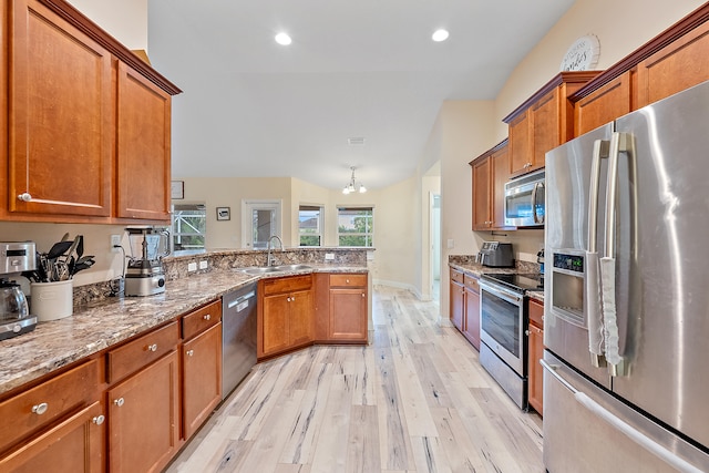 kitchen featuring stainless steel appliances, light hardwood / wood-style floors, sink, kitchen peninsula, and light stone countertops