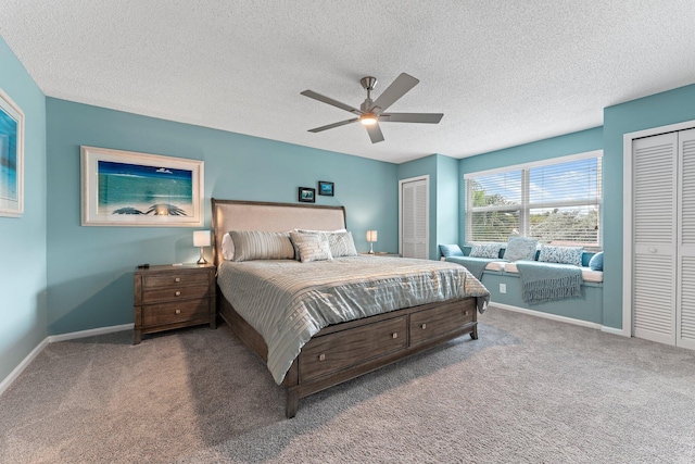 carpeted bedroom with a textured ceiling, ceiling fan, and multiple closets