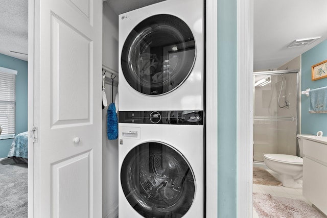 clothes washing area with tile patterned flooring, a textured ceiling, and stacked washer and dryer