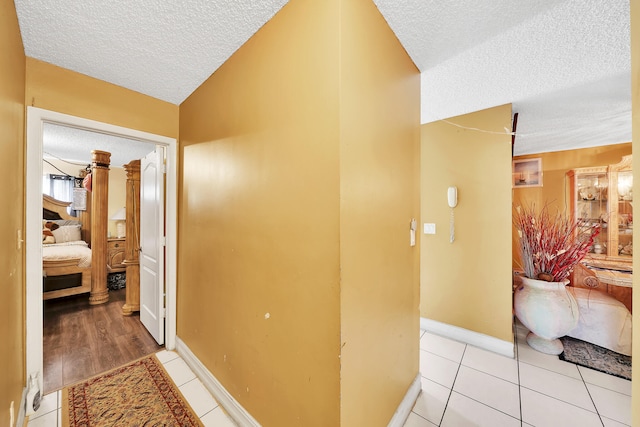 hallway with light wood-type flooring, a textured ceiling, and vaulted ceiling