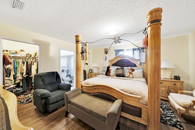 bedroom with a walk in closet, a closet, dark wood-type flooring, and a textured ceiling