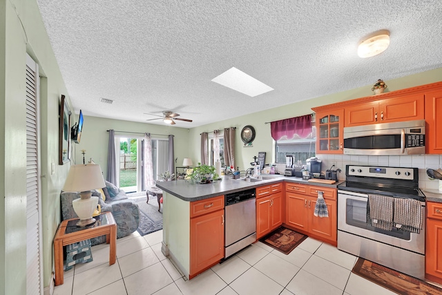 kitchen with kitchen peninsula, backsplash, stainless steel appliances, ceiling fan, and light tile patterned floors