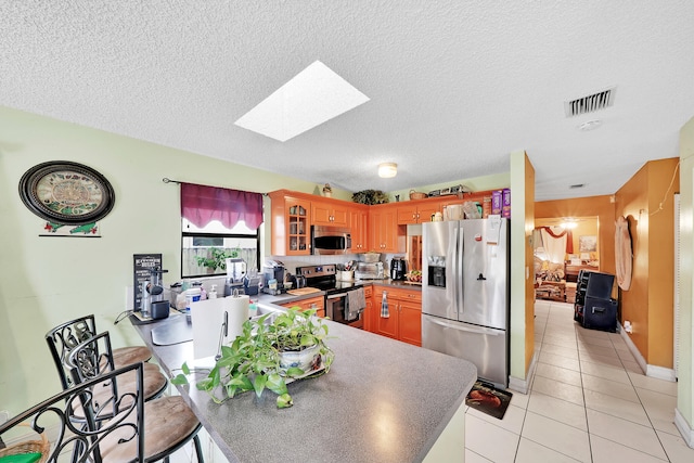 kitchen with kitchen peninsula, appliances with stainless steel finishes, a textured ceiling, and light tile patterned floors