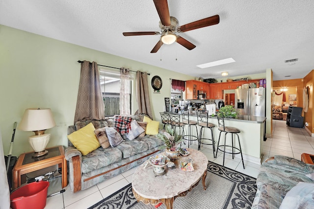 living room with ceiling fan, light tile patterned floors, and a textured ceiling