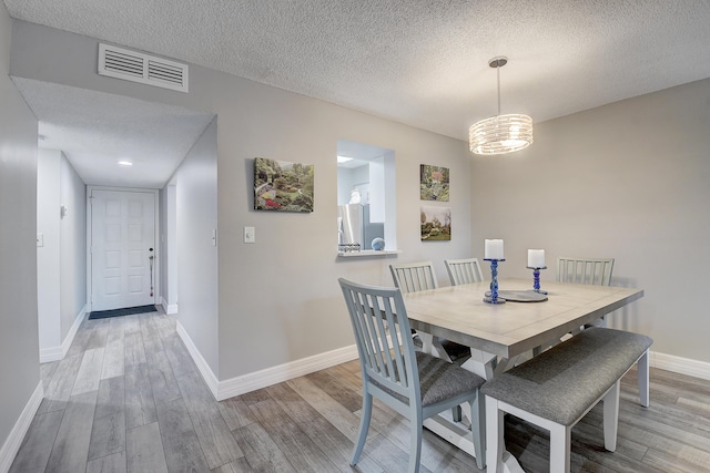 dining room with an inviting chandelier, a textured ceiling, and light wood-type flooring