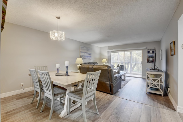 dining area with a textured ceiling, an inviting chandelier, and light hardwood / wood-style flooring