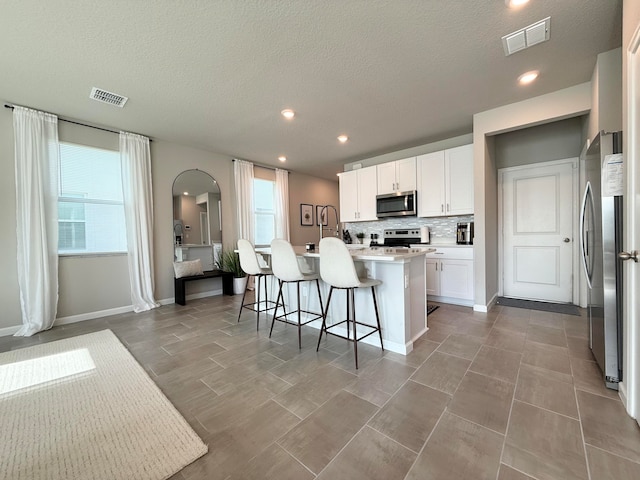 kitchen featuring a center island with sink, white cabinets, a textured ceiling, a kitchen bar, and stainless steel appliances