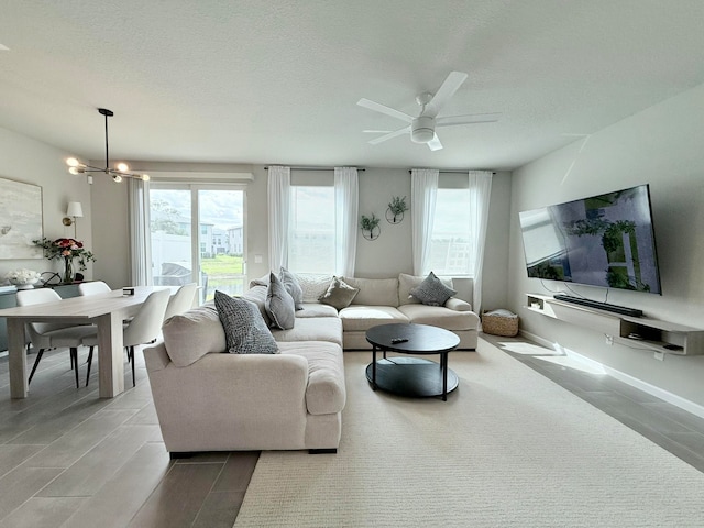 living room with a textured ceiling, plenty of natural light, and ceiling fan with notable chandelier