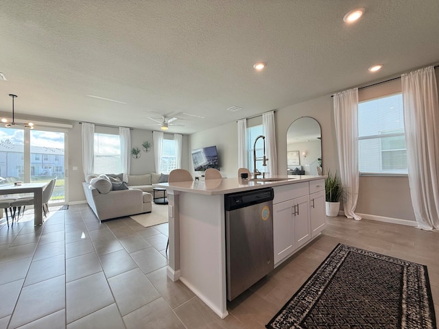 kitchen featuring stainless steel dishwasher, sink, pendant lighting, white cabinetry, and an island with sink