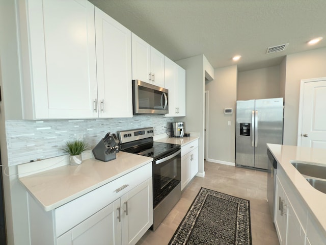 kitchen with white cabinetry, stainless steel appliances, light tile patterned floors, and tasteful backsplash