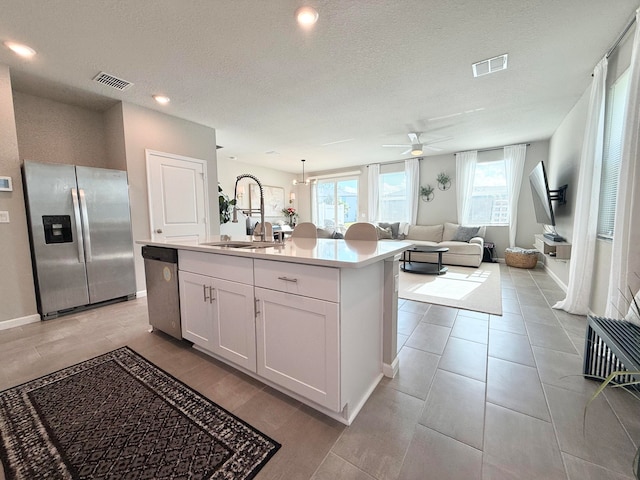 kitchen with a textured ceiling, stainless steel appliances, a kitchen island with sink, sink, and white cabinetry