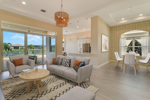 living room with a chandelier, light wood-type flooring, a water view, and sink