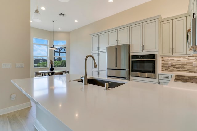 kitchen featuring tasteful backsplash, stainless steel appliances, sink, pendant lighting, and light hardwood / wood-style flooring