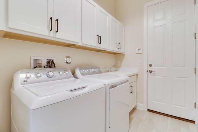 laundry area featuring cabinets, washing machine and dryer, light hardwood / wood-style floors, and sink