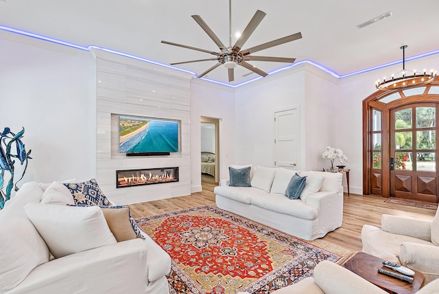 living room with light wood-type flooring, a large fireplace, crown molding, and ceiling fan with notable chandelier