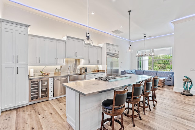 kitchen with stainless steel appliances, wine cooler, decorative light fixtures, sink, and a kitchen breakfast bar