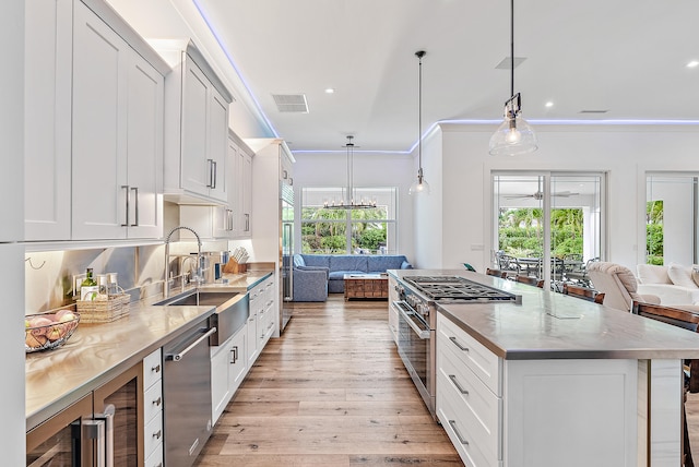 kitchen featuring stainless steel appliances, light wood-type flooring, white cabinetry, hanging light fixtures, and sink