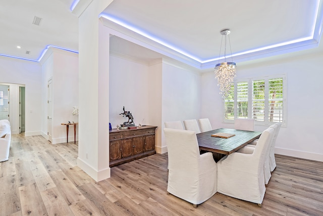 dining space with ornamental molding, an inviting chandelier, light hardwood / wood-style floors, and a raised ceiling