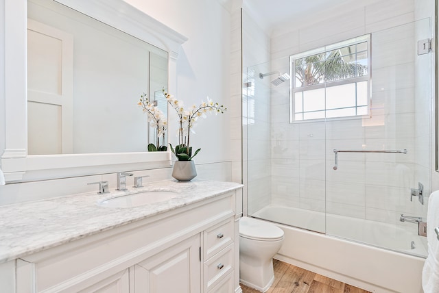 full bathroom featuring hardwood / wood-style floors, vanity, combined bath / shower with glass door, and toilet