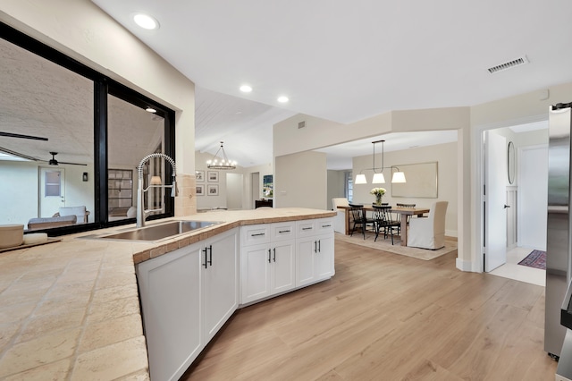 kitchen with white cabinets, sink, pendant lighting, ceiling fan with notable chandelier, and light wood-type flooring