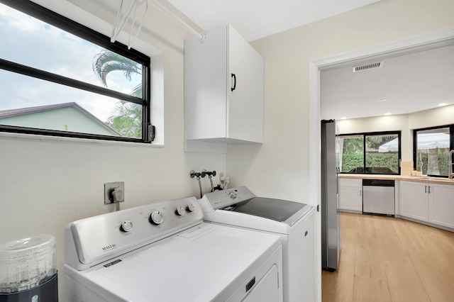 laundry room with washing machine and clothes dryer, cabinets, and light wood-type flooring