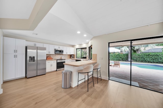 kitchen featuring white cabinetry, stainless steel appliances, a kitchen breakfast bar, kitchen peninsula, and light hardwood / wood-style floors