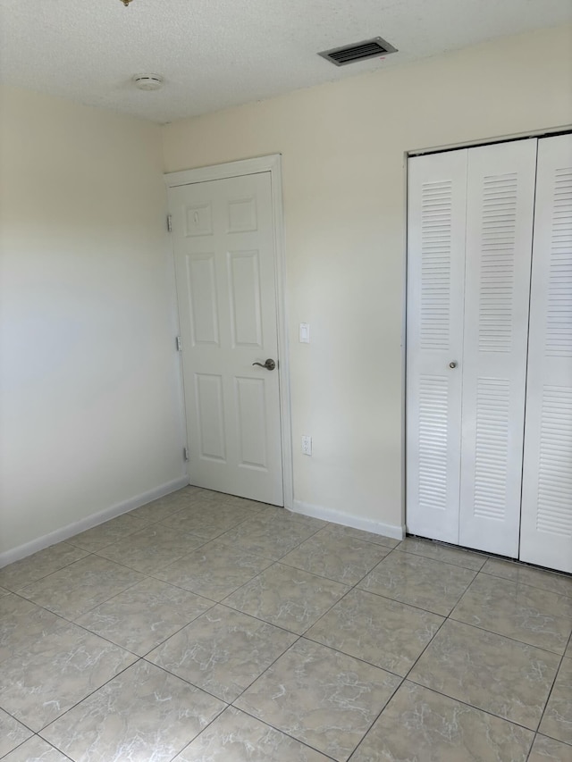 unfurnished bedroom with light tile patterned floors, a closet, and a textured ceiling