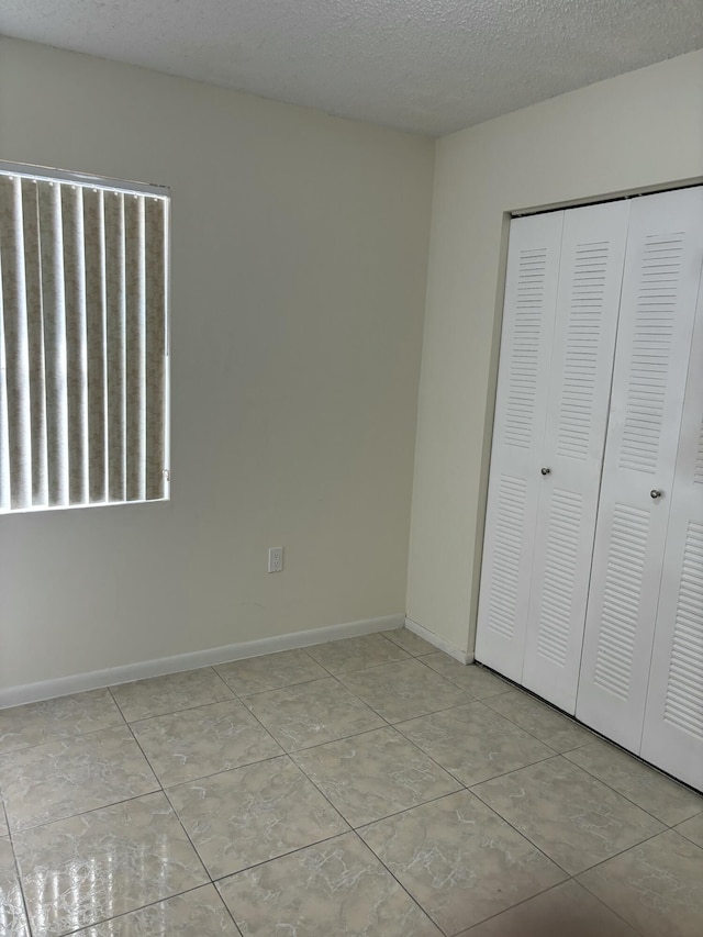 unfurnished bedroom featuring a closet, a textured ceiling, and light tile patterned flooring