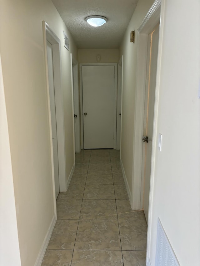 hallway with a textured ceiling and light tile patterned floors