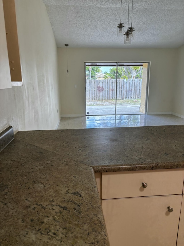 kitchen featuring dark stone counters, decorative light fixtures, a textured ceiling, and light tile patterned floors