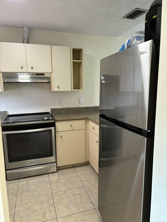 kitchen featuring stainless steel appliances, cream cabinets, light tile patterned floors, and a textured ceiling