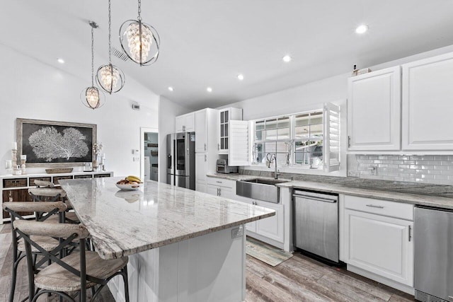 kitchen with pendant lighting, a center island, vaulted ceiling, white cabinetry, and stainless steel appliances