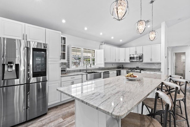 kitchen with a center island, sink, stainless steel appliances, vaulted ceiling, and white cabinets