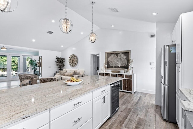 kitchen featuring light stone countertops, stainless steel fridge, beverage cooler, white cabinets, and hardwood / wood-style floors