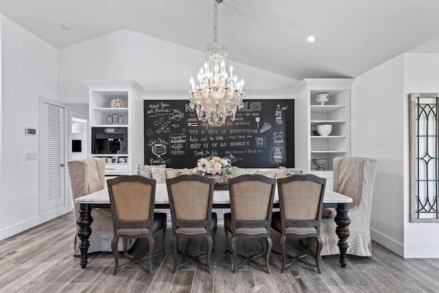 dining room with a notable chandelier, built in features, wood-type flooring, and vaulted ceiling