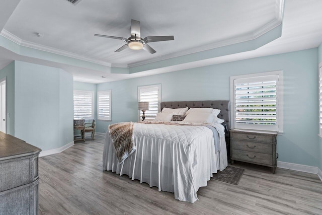 bedroom with a raised ceiling, multiple windows, ceiling fan, and light wood-type flooring