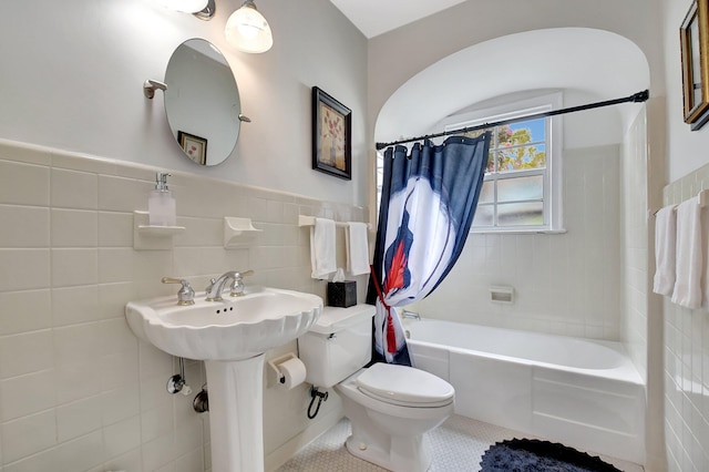 full bathroom with shower / bath combo, toilet, a wainscoted wall, tile patterned floors, and tile walls