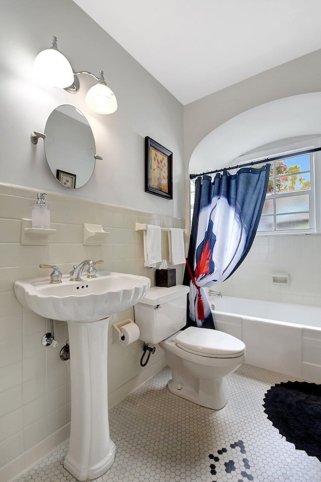 full bathroom with wainscoting, toilet, shower / tub combo with curtain, tile patterned flooring, and tile walls