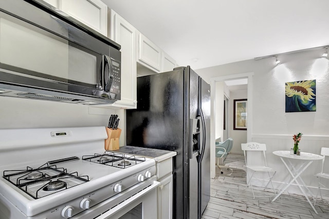 kitchen featuring a wainscoted wall, black appliances, light countertops, and white cabinets