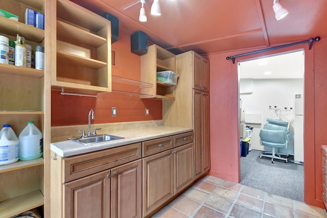 kitchen featuring open shelves, light colored carpet, light countertops, freestanding refrigerator, and a sink