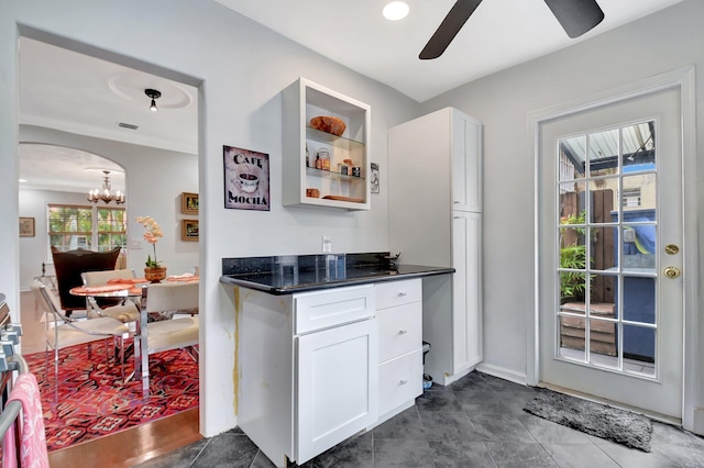 kitchen with arched walkways, a ceiling fan, baseboards, white cabinets, and dark countertops