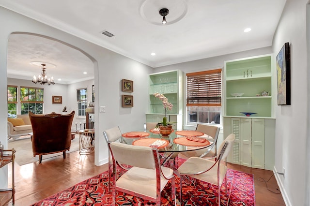 dining area with arched walkways, crown molding, visible vents, wood finished floors, and a chandelier