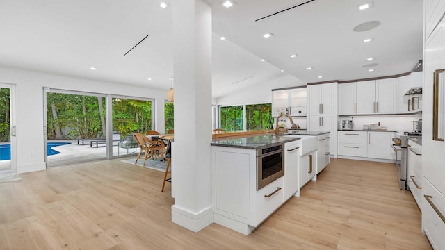 kitchen with white cabinets, lofted ceiling, stainless steel range, and light hardwood / wood-style flooring