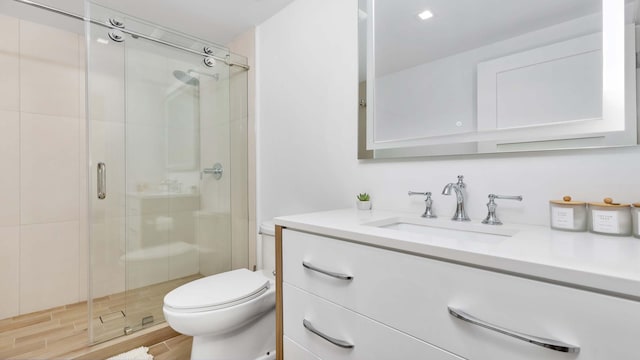 bathroom with hardwood / wood-style floors, vanity, toilet, and a shower with door