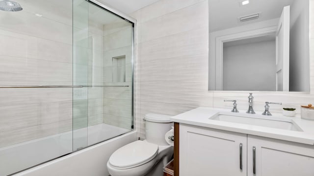 full bathroom featuring decorative backsplash, vanity, shower / bath combination with glass door, tile walls, and toilet