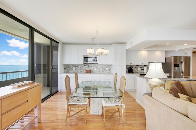 dining area with a chandelier, expansive windows, a water view, and light hardwood / wood-style flooring