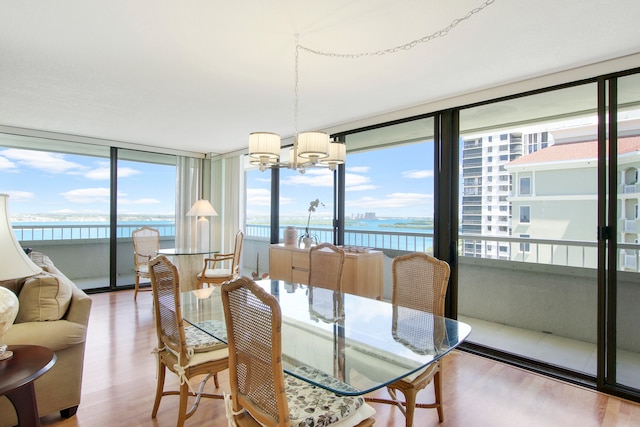 dining space with light hardwood / wood-style floors, a wall of windows, a water view, and a notable chandelier