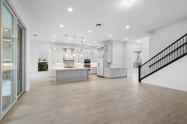 kitchen featuring custom exhaust hood, a center island, paneled refrigerator, decorative light fixtures, and light hardwood / wood-style floors